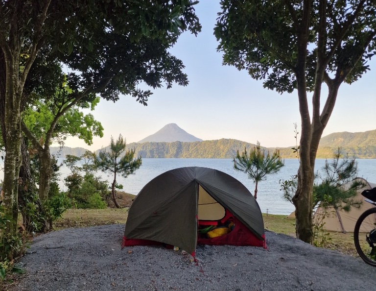 A small camping tent in front of a lake, with a volcano in the background