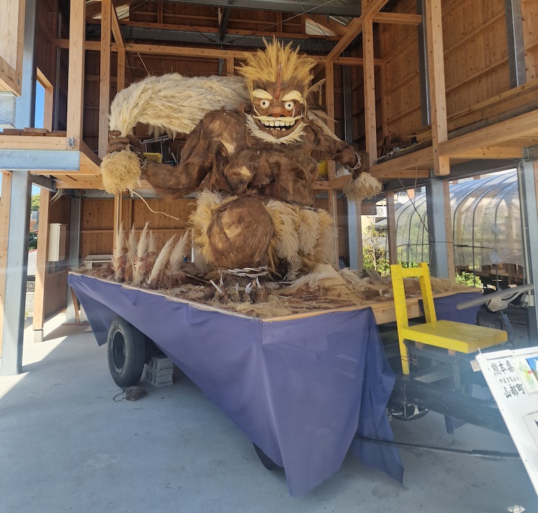 A wooden statue of a troll-like creature holding wheat