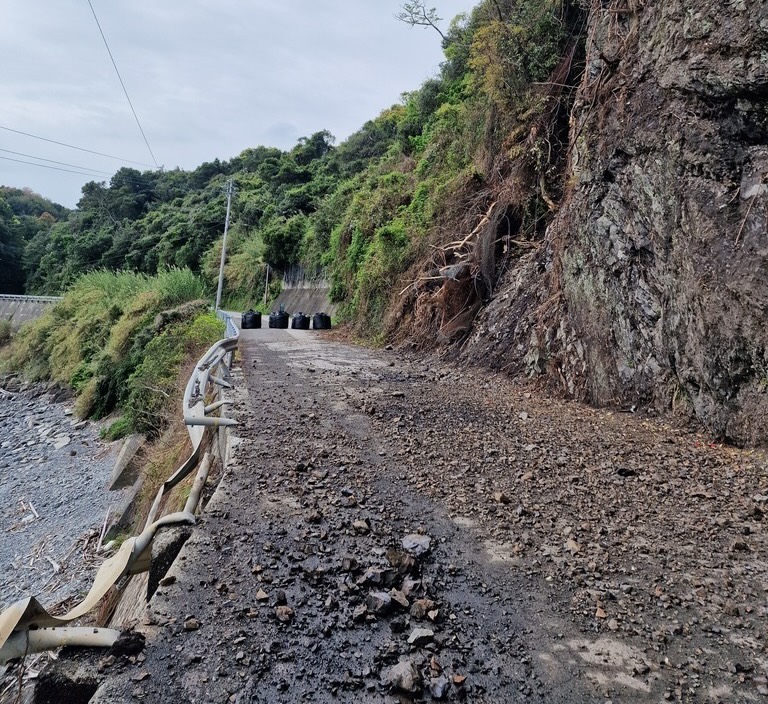 A road with a lot of debris in the roadway, in the distance you can see the road is closed with some huge black bags