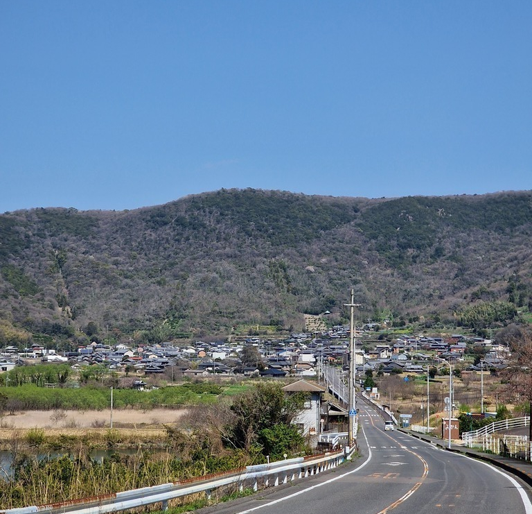 A nearly straight road going towards a hill, through a small village