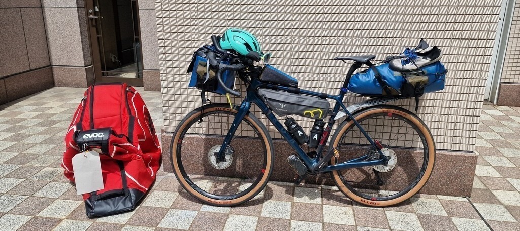 My gravel bike next to my red bike suitcase outside a brick wall