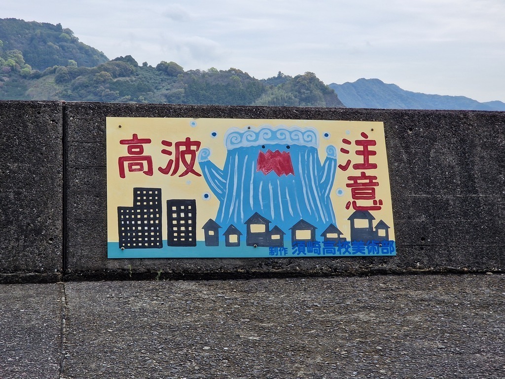 A hand painted sign of a wave with a big red mouth towering over a city