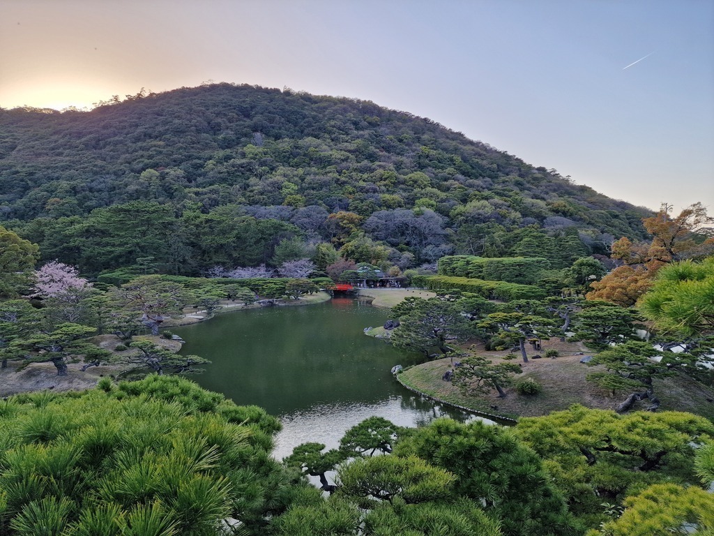 A picture of the old royal garden Ritsurin, with a beautiful forest hill in the background, while the sun goes down