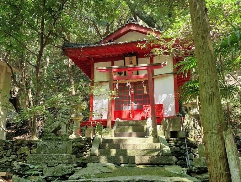 A red shrine on top of a stone stair case, hidden between the trees