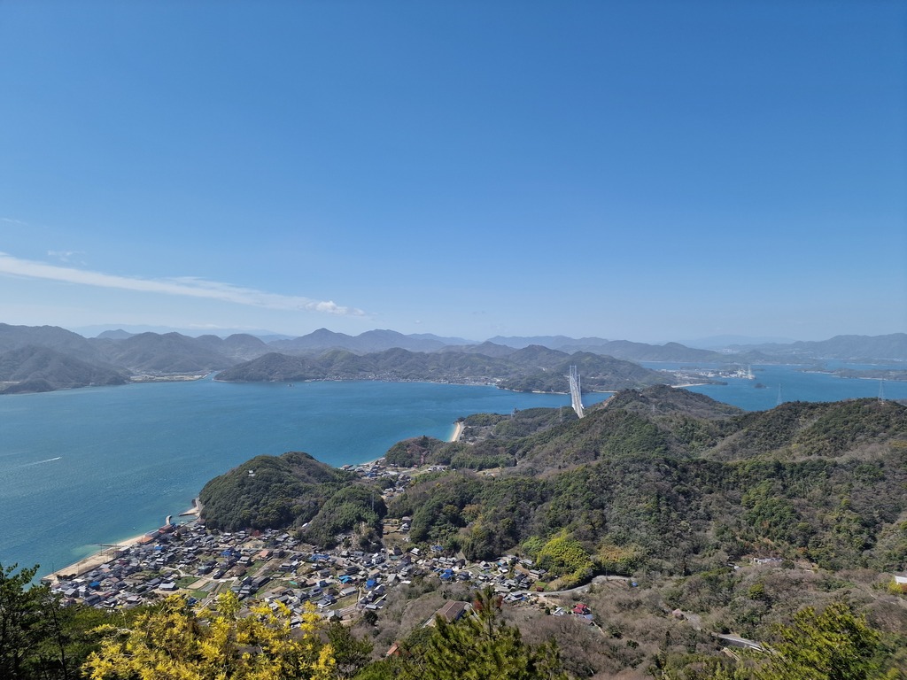 View of a bridge connecting two island with a lot of forest, you can see a small town at the bottom of the image.